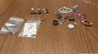 Full lot image showing all jewelry items laid out on wooden surface, including rings, pendants, scarf clip, and pins