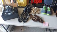 Wide shot of all shoes and boots on a table including New Balance runners, heeled sandals, thong sandals, beige boots, and black heeled shoes.