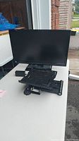 Front view of the 24-inch Fluid TV with built-in DVD player at the back, placed on a white table outdoors, with remote control on top of DVD player.