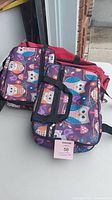 Top view of two colorful owl patterned lunch bags stacked together with black handles visible.