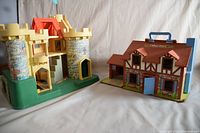 Photo showing both the vintage Fisher Price Castle and House side by side on a white cloth. Each item is fully visible for comparison and condition review.