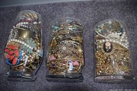 Photo displaying three large glass jars full of assorted mixed jewelry including necklaces, bracelets, rings, and colorful jewelry-making supplies.