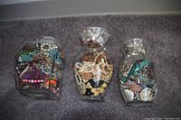 Three large glass jars filled with mixed jewelry including colorful beads, wooden beads, chains, and earrings.