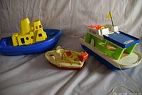 Set of three vintage toy boats on white fabric background: Fisher Price Play Family Boat, squeeze tug boat, Lakeside boat.