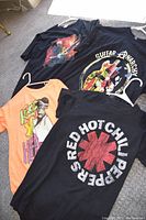 All four T-shirts laid out and visible: Red Hot Chili Peppers, Tupac, Eric Clapton, and Guitar Anarchy designs.