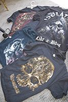 Four black medium-large size graphic T-shirts spread on the floor showing skull and grim reaper graphics