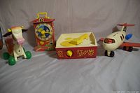 Photo showing all four vintage Fisher Price toys placed side by side: Molly Moo Cow, Teaching Clock, Music Box Record Player, and Airplane Funjet.