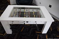 Full view of cocktail style foosball table with white frame and glass top in room setting.