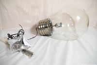 Photo showing the large, clear glass bulb shaped as a giant light bulb with a metal screw base and attached wiring.