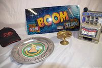 Full lot showing items: Riviera casino hat, Great Seal aluminum plate, BOOM Williams 1997 slot machine glass, Carousel Bank slot machine, Mexican Centavo coin ashtray.