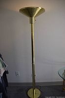 Full view of tall brass floor lamp with round base and upward-facing shade.