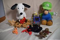 Wide shot of the lot showing the large Snoopy plush, Luigi plush figure, mini BurgerTime arcade machine, and various small plush and beanie animals scattered around.