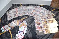 Wide view of basketball cards in protective sleeves inside a binder along with a pile of loose cards spread out on a carpet.