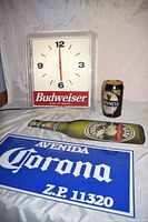 Photo of Budweiser clock, Corona metal sign, Guinness can, and Moosehead metal bottle sign together on white surface.