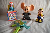 Photo showing Fisher Price Jolly Jumping Jack, 1950s mouse bank, Mattel Jack in the Box, and Pinocchio bank all together on flat surface.
