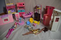 Photo showing the complete set of vintage large doll house appliances, household furniture, two dolls, and a miniature bicycle arranged on a beige surface.