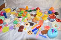 Wide view of colorful vintage plastic toy food and kitchenware items laid out, showing various items like toy eggs, cookies, breads, and dishes.