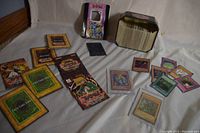 Photo showing the metal tin case filled with Yu-Gi-Oh! cards, some holographic cards in protective sleeves, booster packs, and loose cards spread out.