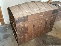Full side view of the antique steamer trunk showing the domed top, vertical wooden slats, metal reinforcements, and attached latches.