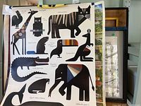 Photo showing a large poster print with various stylized animal silhouettes including giraffe, cat, owl, crocodile, elephant, whale, and more with colorful textured patterns composed of fabric swatches.