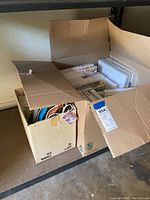 Overview of two open cardboard boxes containing assorted artist canvases, photo frames, and gift bags.