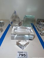 Clear acrylic decorative art pieces arranged on a white surface, including a rectangular block with recessed oval shape, triangular prisms, and a square block.