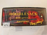 Original box showing the text 'Doodlesack Miniature Bagpipes They play!' and the tartan miniature bagpipes visible inside.