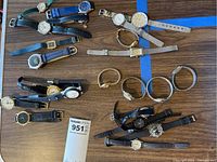 Overview of all 15 watches, various styles and colors laid out on a wooden surface, showing strap materials and watch faces.