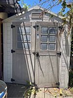 Front view of light gray resin shed showing double swing doors with molded window panels