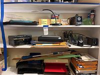 Shelf view showing Logan light box, tin chest, paper cutter, stacked photo paper, and various desk supplies such as staplers and pencils.