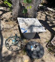 Photo showing the square marble top resting on the large round pot base, with two metal umbrella stands placed nearby.