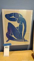 Front view showing blue nude print in plastic box frame resting on a shelf with visible frame cracks and some warping on artwork.