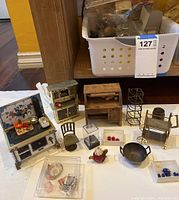 Miniature dollhouse furniture and household items arranged on a table, including stoves, chairs, cupboards, and various small accessories.