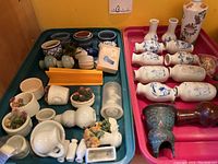 Photo showing multiple small ceramic pots of different shapes and decorations arranged in two plastic trays, alongside larger blue and white vases and one tall floral vase.