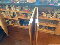 Photo of open cabinets showing shelves filled with ceramic mugs of various designs and styles, plastic cups, and clear glassware.