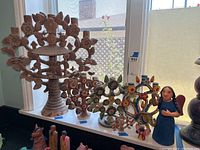 Wide view of five Mexican folk art pottery items on windowsill including three Tree of Life candle holders and two angels.