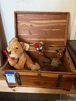 Wooden chest with open lid, containing three plush toys: a dog, zebra, and reindeer.