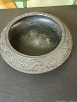 Top front perspective view of a dark vintage ceramic bowl showing intricate carved patterns on the rim and a worn interior surface.