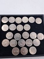 Twenty-two Canadian dollar coins arranged on black display surface showing front sides and various dates and designs from the 1970s, including commemorative Winnipeg 100 coins.
