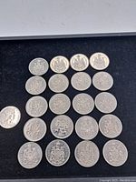 Overhead view of 19 Canadian 50 cent coins arranged in rows on a black felt background showing the reverse sides with the coat of arms.