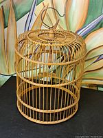 Full view of the wooden birdcage showing cylindrical shape, vertical slats, top finial and metal hook for hanging.