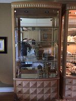 Front view of tall wooden display cabinet with glass doors showing the glass shelves inside and decorative wooden drawers below