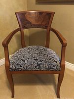 Front view of the wooden armchair showing the backrest with decorative wood inlay and curved wooden arms.