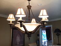 Chandelier hanging from ceiling in room, showing six arms with lampshades and central glass bowl.