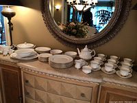 Wide view of china set arranged on marble-top sideboard beneath mirror, showing plates, tea set and serving pieces