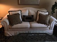 Front view of white upholstered couch with five decorative pillows, two largest pillows on outer ends and three center pillows.