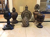 Front view showing six decorative urns and finials arranged in a row on a tile floor in front of a mirror.