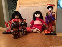 Full collection of six Japanese dolls displayed on a table showing the variety and condition of the dolls.