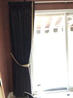 Two dark drapery panels with beige geometric pattern and beige tiebacks on window in a sunlit room