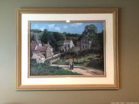 Full view of the framed artwork showing a peaceful rural village scene with multiple stone houses and a dirt path, matted and framed in gold-tone.